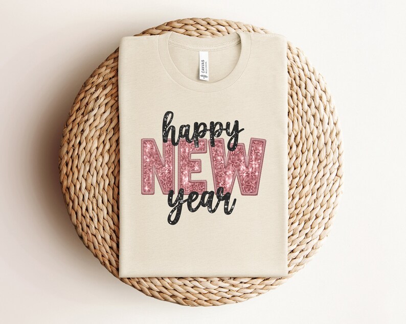May include: A white t-shirt with the words "happy new year" printed on it in black and pink glitter. The word "new" is in pink glitter and the rest of the text is in black.
