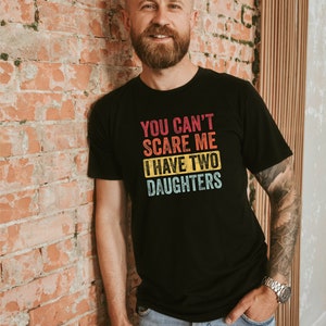 Puede incluir: Una camiseta negra con un gr&aacute;fico de estilo vintage que dice "You can't scare me I have two daughters".