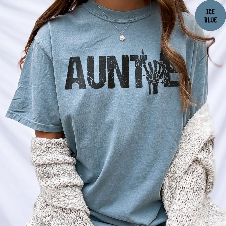 May include: Ice blue t-shirt with the word "AUNT" in bold black letters, followed by a graphic of a hand making a rude gesture. The shirt is a light blue color and has a casual, relaxed fit.