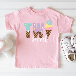 May include: Pink t-shirt with the text "TWO sweet" and a graphic of two ice cream cones with sprinkles.