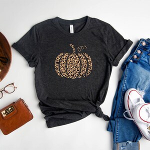 May include: A dark heather gray t-shirt with a leopard print pumpkin graphic and the text "Sister from another mother".