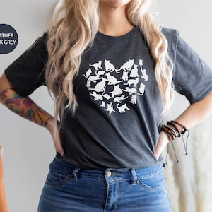 May include: A heather dark grey t-shirt with a white graphic of a heart made of cats. The text "Ojev Apparel Soft Quality Clothing" is visible in the upper right corner of the image.