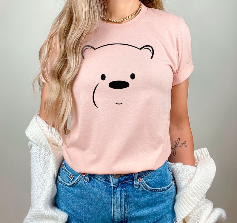 May include: A pink t-shirt with a black outline of a bear's face. The bear has a small black nose and two black eyes.