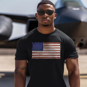 Pode incluir: Uma camiseta preta com um gr&aacute;fico de bandeira americana de estilo vintage impresso na frente. A bandeira &eacute; vermelha, branca e azul com um visual desgastado.