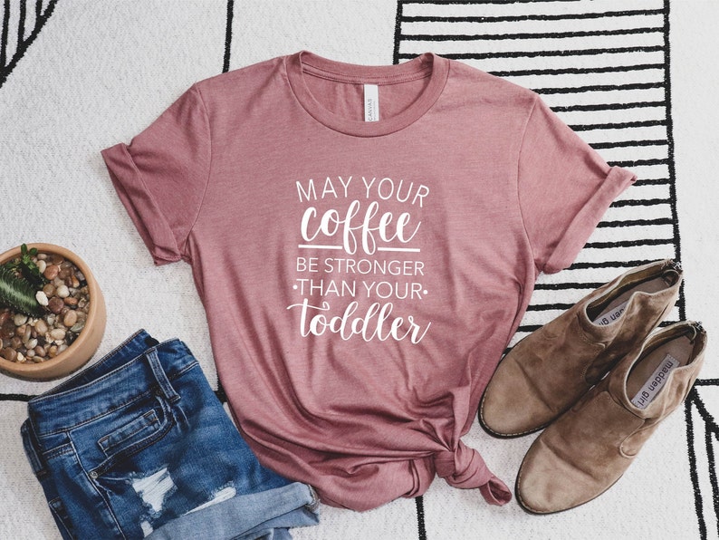 May include: A mauve t-shirt with the text "May your coffee be stronger than your toddler" printed in white.