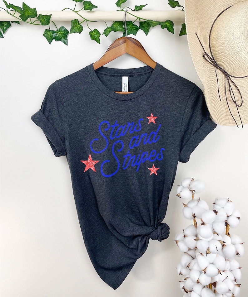 May include: A dark gray t-shirt with the text "Stars and Stripes" in blue glitter lettering and red glitter stars.