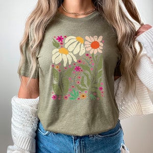May include: A green t-shirt with a floral print featuring white, pink, orange, and yellow flowers. The flowers are surrounded by green leaves and stems.