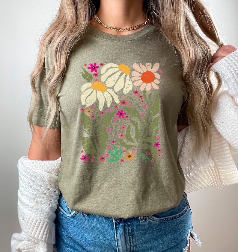 May include: A green t-shirt with a floral print featuring white, pink, orange, and yellow flowers. The flowers are surrounded by green leaves and stems.