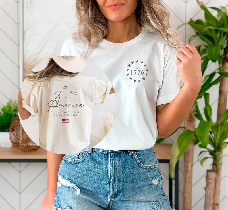 Peut inclure: Un t-shirt blanc avec un graphique sur le devant qui dit "Since 1776" avec un cercle d'&eacute;toiles autour du texte. Le dos du t-shirt a un graphique qui dit "The United States of America, The Land of the Free, The Home of the Brave" avec un petit drapeau am&eacute;ricain.
