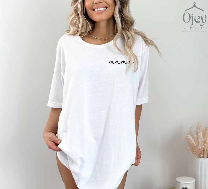 以下が含まれることがあります： 前面に黒い筆記体で「mama」と書かれた白いオーバーサイズのTシャツです。