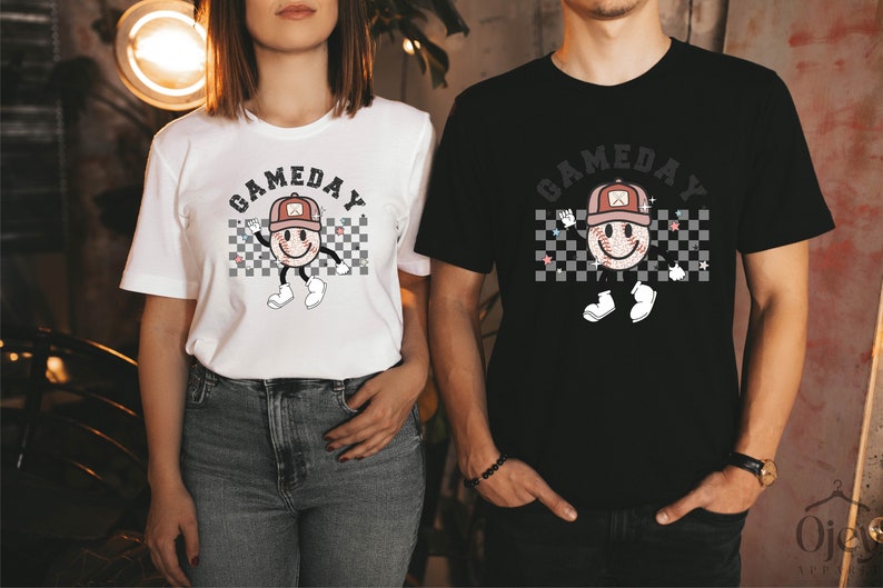 May include: Two people wearing white and black t-shirts with a graphic of a smiling baseball with a hat and the text "GAMEDAY" printed on the front.