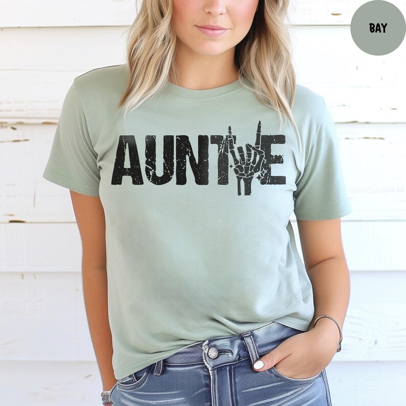 May include: A light green t-shirt with the word "AUNTIE" in distressed black lettering. The letter "E" is replaced with a hand gesture. The shirt is made of a soft material and is a casual style.