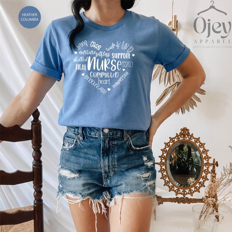 May include: A light blue t-shirt with a white heart design featuring the word "NURSE" surrounded by words describing the qualities of a nurse. The text reads: "strong care touch & kind nurture selfless support skilled heal NURSE respect committed heart compassion encourage"