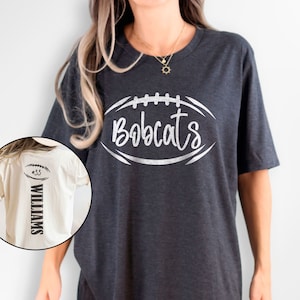 May include: A dark grey t-shirt with a white football graphic that says "Bobcats". A white t-shirt with a black football graphic and the text "#33 WILLIAMS" is shown in the background.