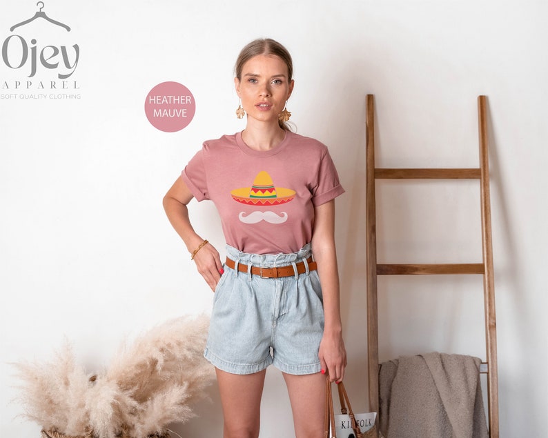 May include: A heather mauve t-shirt with a graphic of a sombrero and a mustache. The text "HEATHER MAUVE" is visible in the top left corner of the image.