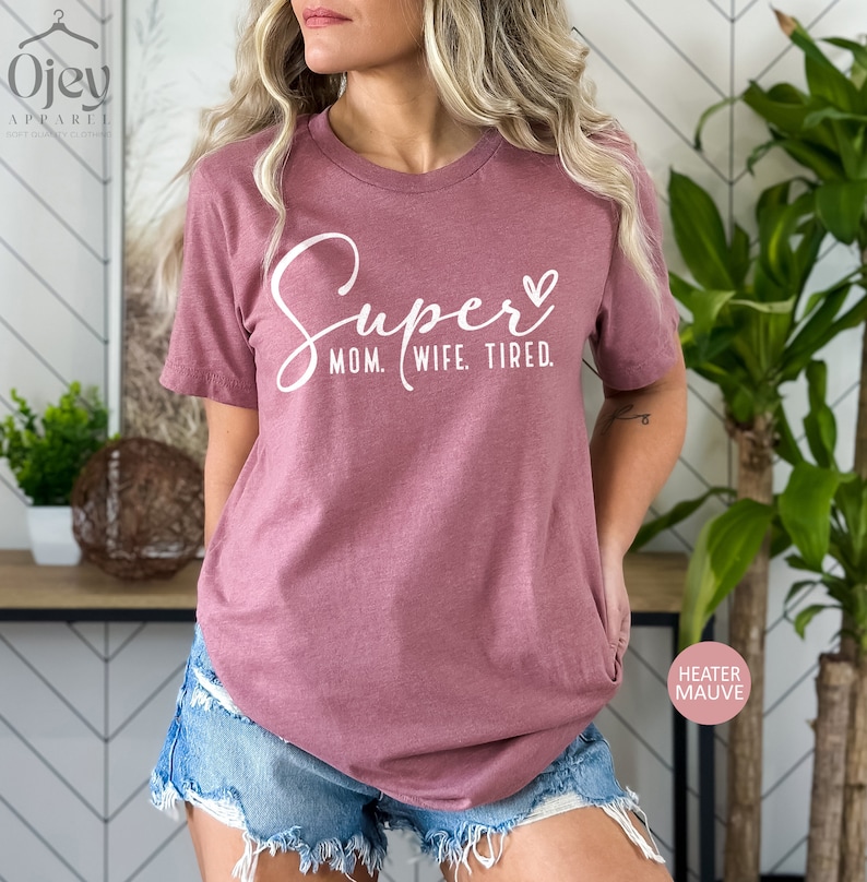 May include: A mauve t-shirt with the text "Super Mom. Wife. Tired." in white lettering and a small heart.