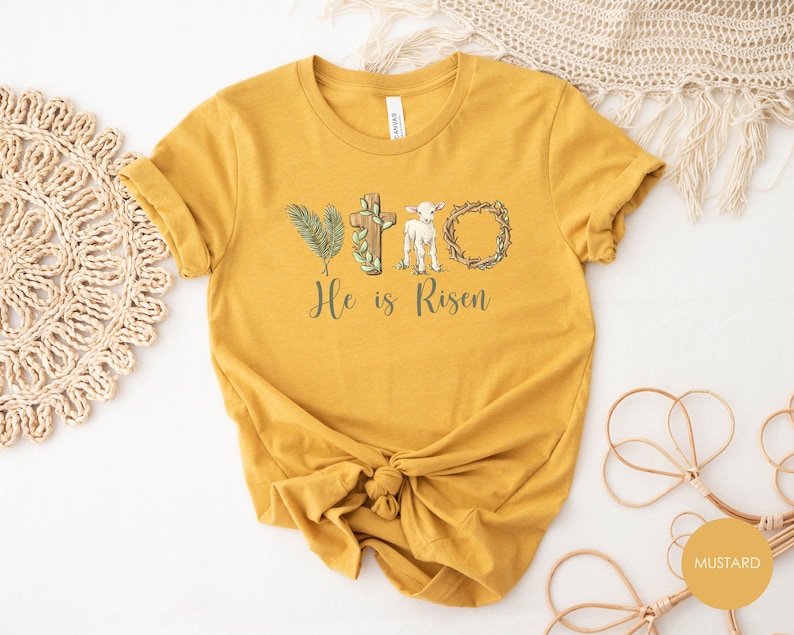 May include: Mustard yellow t-shirt with a graphic of a cross, palm branches, a lamb, and a crown of thorns. The text "He is Risen" is printed below the graphic.