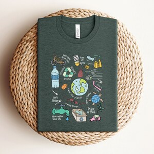 May include: A dark green t-shirt with a colorful illustration of ways to help save the planet. The illustration includes a bicycle, a water bottle, a recycling symbol, a globe, a turtle, a tree, and the words "Recycle, Reduce, Reuse, Save the Planet, Plant a Tree, Don't Litter, Save Water, Save Life".