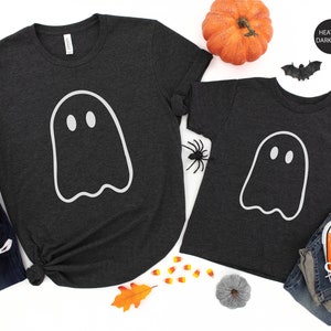 May include: Two heather dark grey t-shirts with a white ghost graphic. The larger shirt has the text "Ojew Apparel" on the top left corner. The smaller shirt has the text "Heather Dark Grey" on the top right corner.