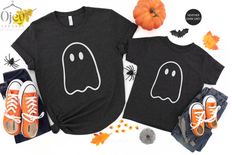 May include: Two heather dark grey t-shirts with a white ghost graphic. The larger shirt has the text "Ojew Apparel" on the top left corner. The smaller shirt has the text "Heather Dark Grey" on the top right corner.