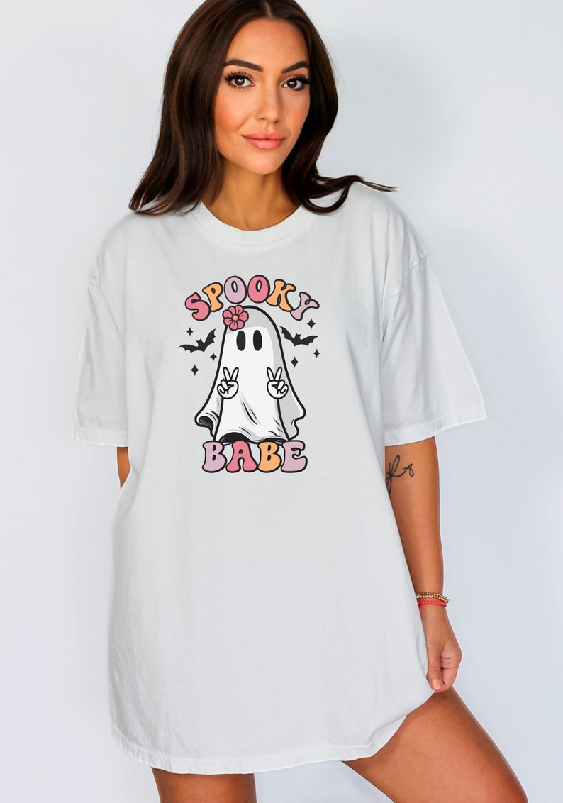May include: White oversized t-shirt with a graphic of a ghost wearing a flower and making the peace sign. The text "SPOOKY BABE" is written in colorful letters.