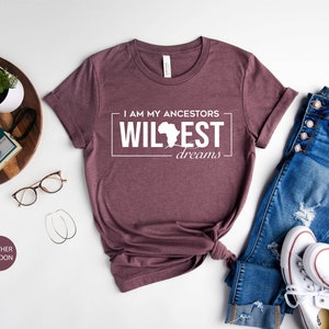 Peut inclure: Un t-shirt en marron chin&eacute; avec le texte "I am my ancestors wildest dreams" et un contour du continent africain.