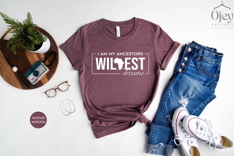 Peut inclure: Un t-shirt en marron chin&eacute; avec le texte "I am my ancestors wildest dreams" et un contour du continent africain.
