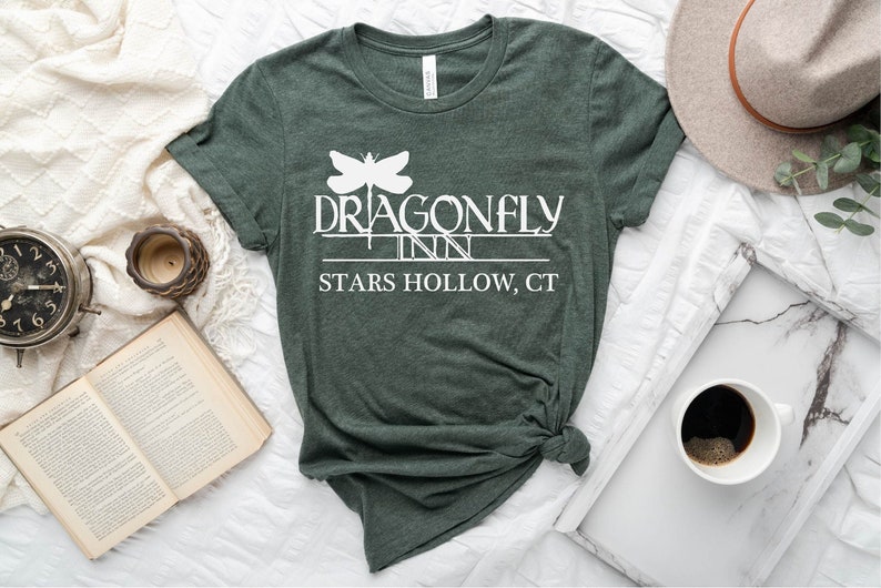 May include: A dark green t-shirt with a white graphic of a dragonfly and the text "Dragonfly Inn Stars Hollow, CT".