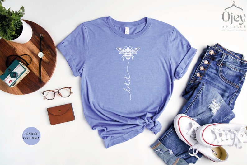May include: A heather columbia blue t-shirt with a white bee graphic and the text "let it" printed on the front.