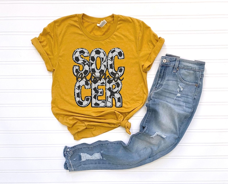May include: A mustard yellow t-shirt with a graphic of a soccer ball pattern that reads "Soccer Mom".