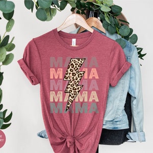 Op de afbeelding: Een heide-frambozen t-shirt met het woord "MAMA" vijf keer herhaald in een verloop van roze, oranje en grijs. Een luipaardprint bliksemgrafiek is gecentreerd op het shirt.