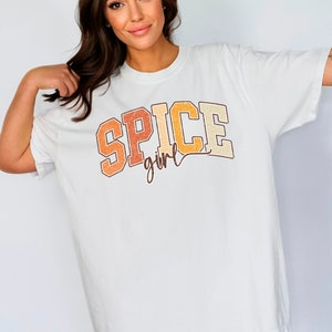 May include: White oversized t-shirt with a vintage-style graphic that says "SPICE girl" in orange, yellow, and brown.