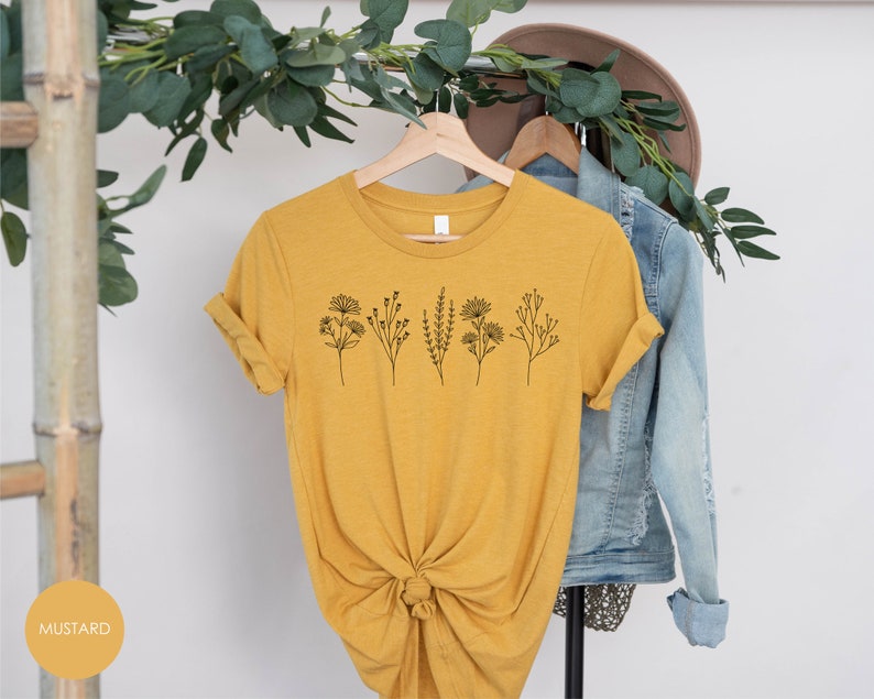 May include: A mustard yellow t-shirt with a simple line drawing of five different flowers on the front.