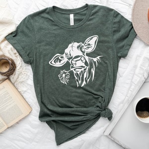 May include: A green t-shirt with a white silhouette of a cow's head with a flower in its mouth.