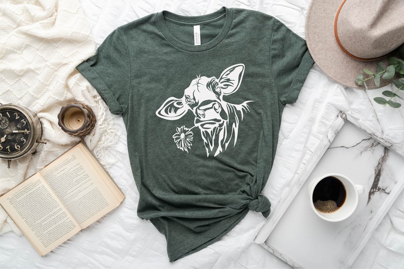 May include: A green t-shirt with a white silhouette of a cow's head with a flower in its mouth.