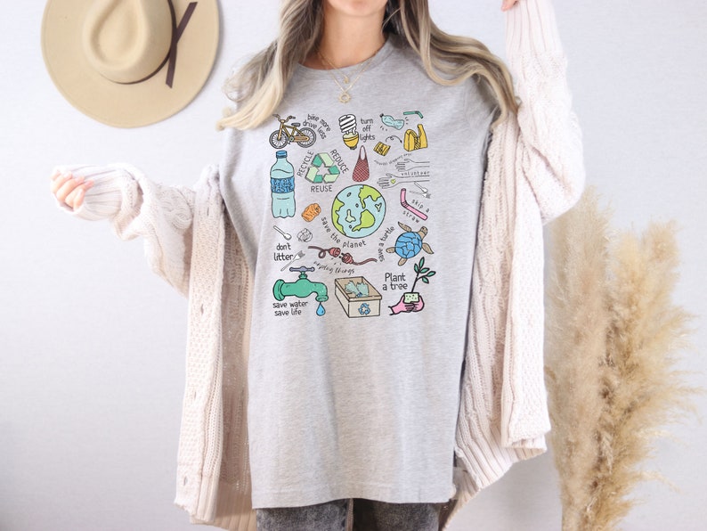 May include: A gray t-shirt with a colorful graphic design featuring various environmental messages and illustrations, including a globe, a turtle, a tree, a faucet, and the words "Recycle, Reduce, Reuse, Save the Planet, Don't Litter, Save Water, Save Life, Plant a Tree".