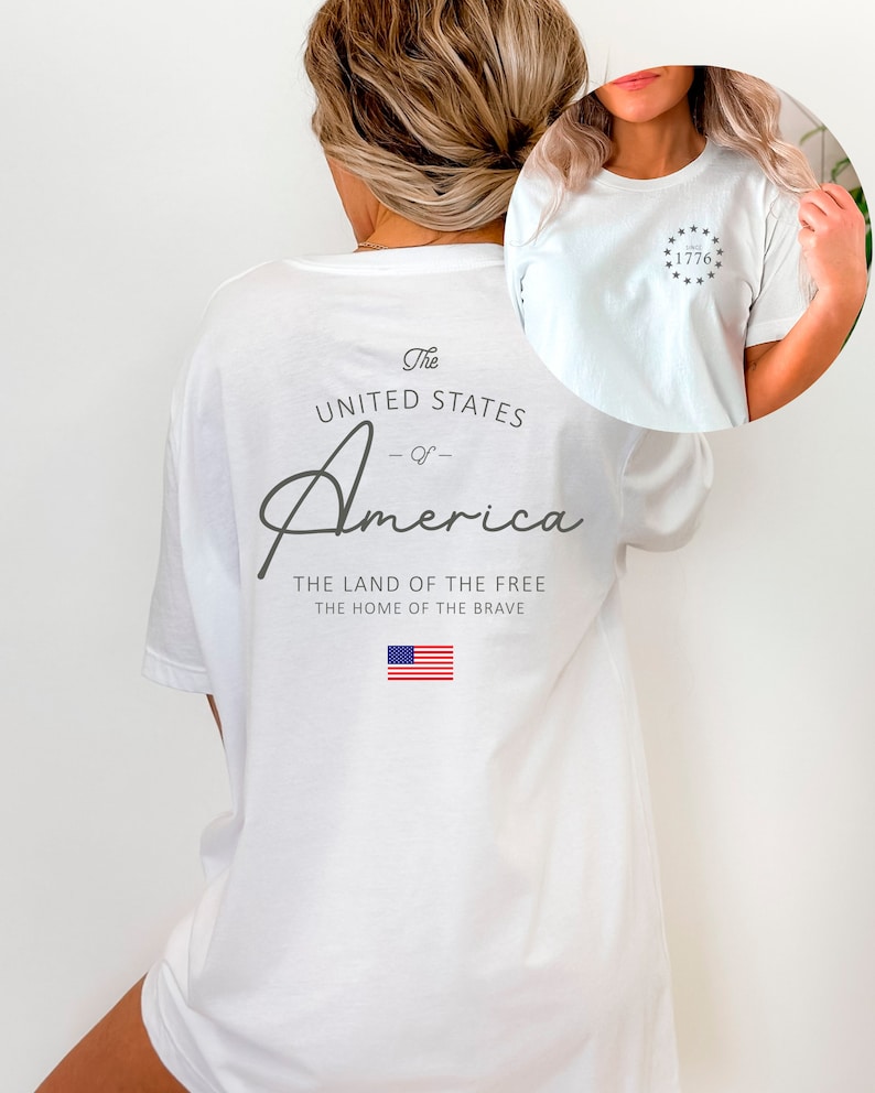 Peut inclure: T-shirt blanc avec un imprim&eacute; graphique des mots "The United States of America" et le texte "The Land of the Free, The Home of the Brave". Le graphique comprend &eacute;galement un petit drapeau am&eacute;ricain. L'avant du t-shirt a un petit graphique d'un cercle avec des &eacute;toiles et le nombre "1776" &agrave; l'int&eacute;rieur.