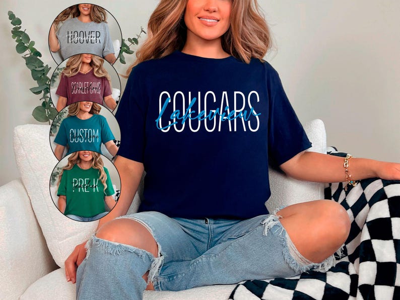 以下が含まれることがあります： 白で「COUGARS」、青で「Lakeview」と書かれたネイビーブルーのTシャツ。画像には、「HOOVER」、「SCARLET OAKS」、「CUSTOM」、「PRE-K」という言葉が書かれた他の4つのTシャツも表示されています。