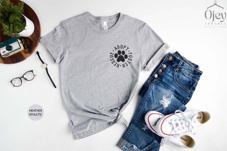 May include: A heather grey t-shirt with a paw print graphic and the text "Adopt Foster Rescue" in a circle around the paw print.
