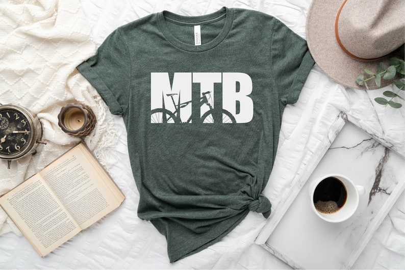 Puede incluir: Una camiseta verde oscuro con la palabra "MTB" en letras blancas. Las letras est&aacute;n formadas por la silueta de una bicicleta de monta&ntilde;a.