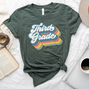 May include: A green t-shirt with the text "Third Grade" in a retro rainbow design.