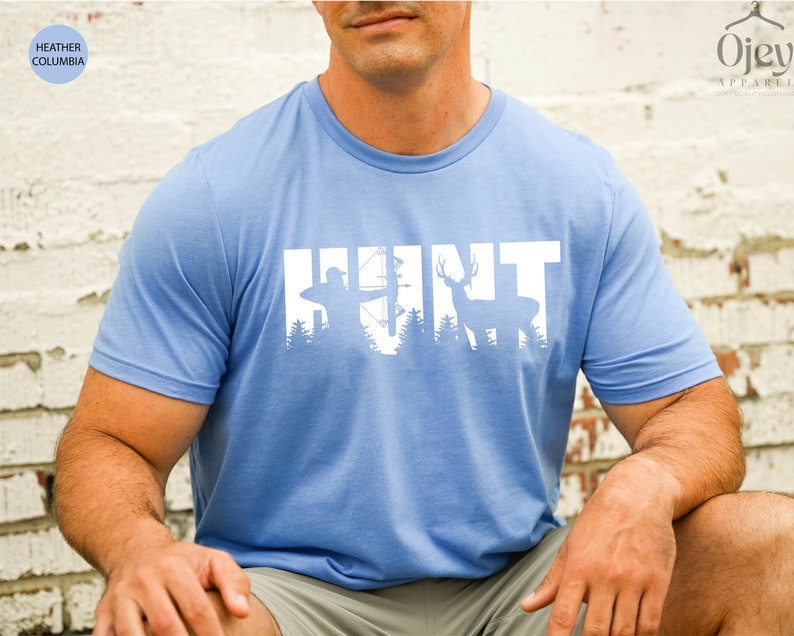 May include: A light blue t-shirt with a white silhouette of a hunter with a bow and arrow and a deer in front of a forest. The word "HUNT" is spelled out with the silhouettes.