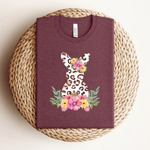 May include: A maroon t-shirt with a white and brown leopard print bunny silhouette with pink, yellow, and orange flowers.