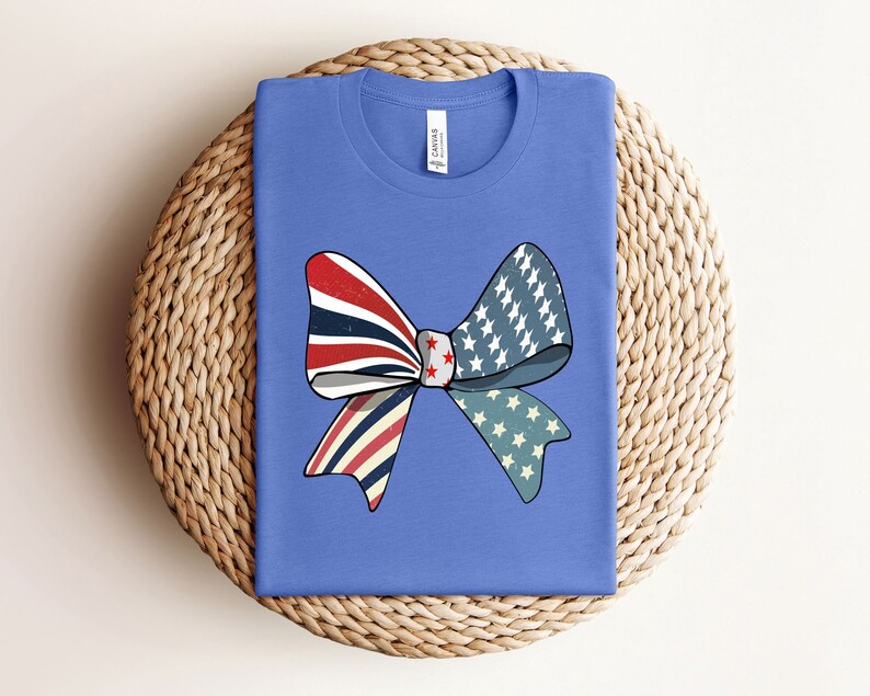 May include: A blue t-shirt with a red, white, and blue bow design. The bow is made of fabric with a stars and stripes pattern.