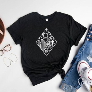 May include: A black t-shirt with a white graphic of a desert scene with cacti and a sun. The graphic is in a diamond shape.