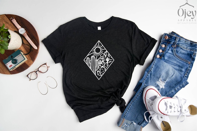 May include: A black t-shirt with a white graphic of a desert scene with cacti and a sun. The graphic is in a diamond shape.