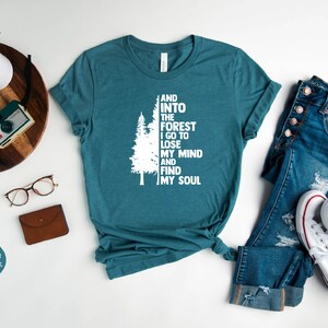May include: A teal heather deep teal t-shirt with a white graphic of a tree and the text "And into the forest I go to lose my mind and find my soul".