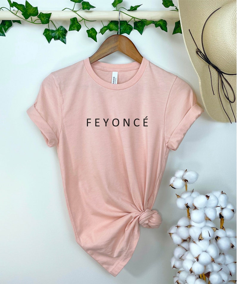 Pu&ograve; includere: Una maglietta rosa chiaro con la scritta "FEYONC&Eacute;" stampata in nero sul davanti.