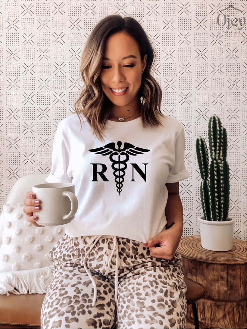 May include: White t-shirt with a black medical caduceus symbol and the letters "RN" printed on the front. The person is wearing leopard print pants.