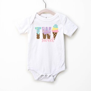 May include: White short-sleeved bodysuit with the text "TWO sweet" in pink letters. The "TWO" is made up of ice cream cones with sprinkles and a pink, yellow, and blue ice cream scoop.